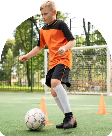 Young soccer player in orange and black uniform dribbling a ball through training cones.